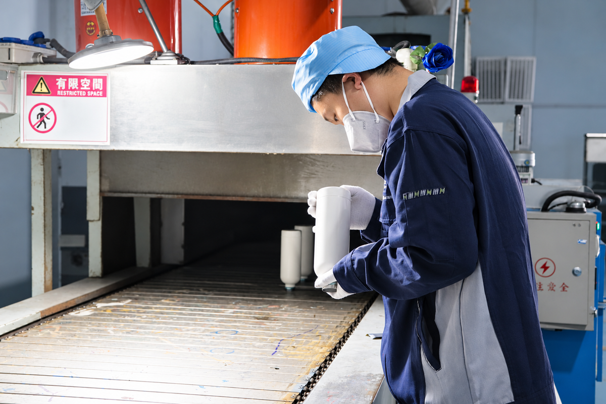 Operator checking a drinkware cup for surface defects under inspection lighting